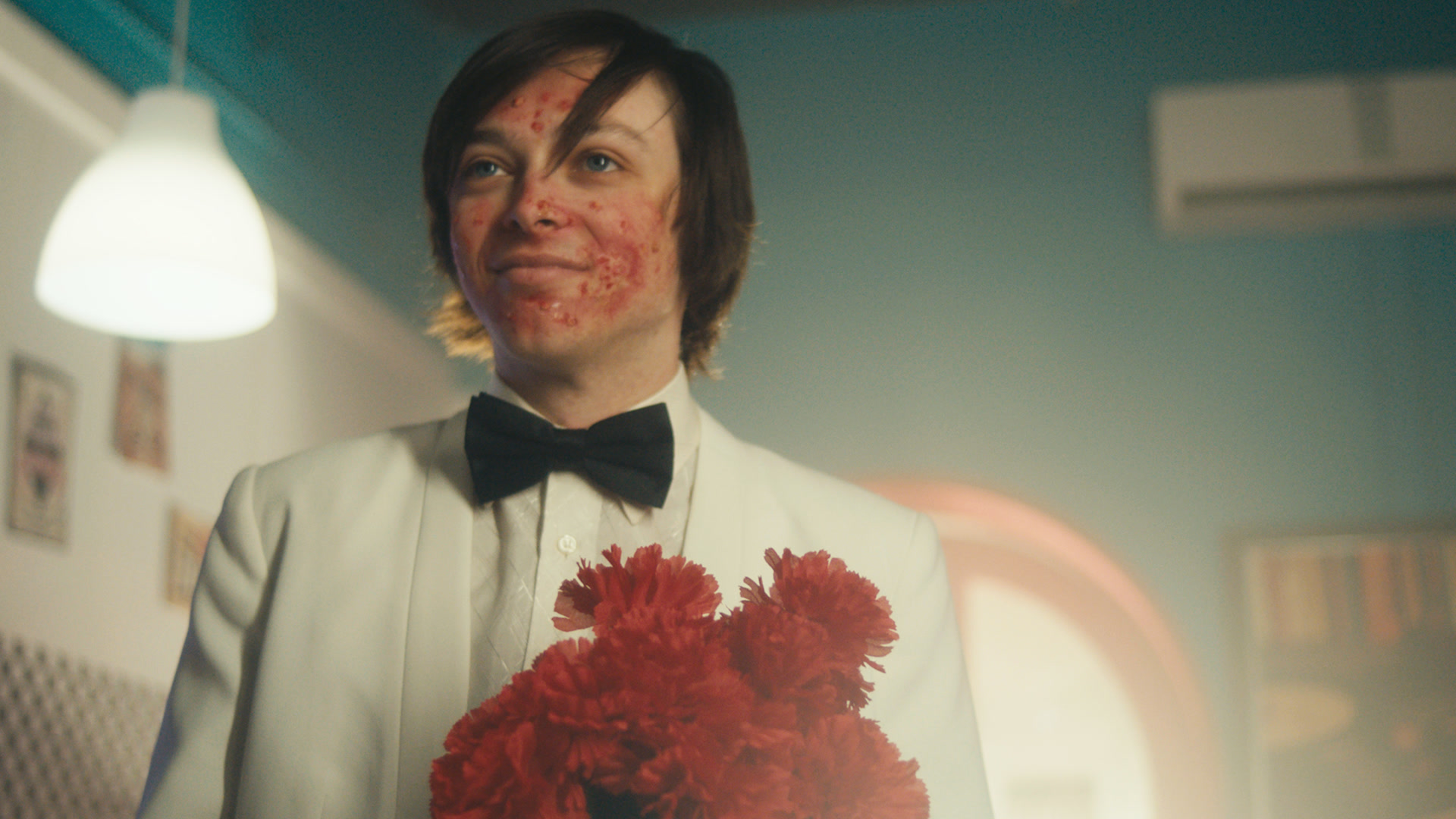 A man in a white suit and black bow tie holding red flowers