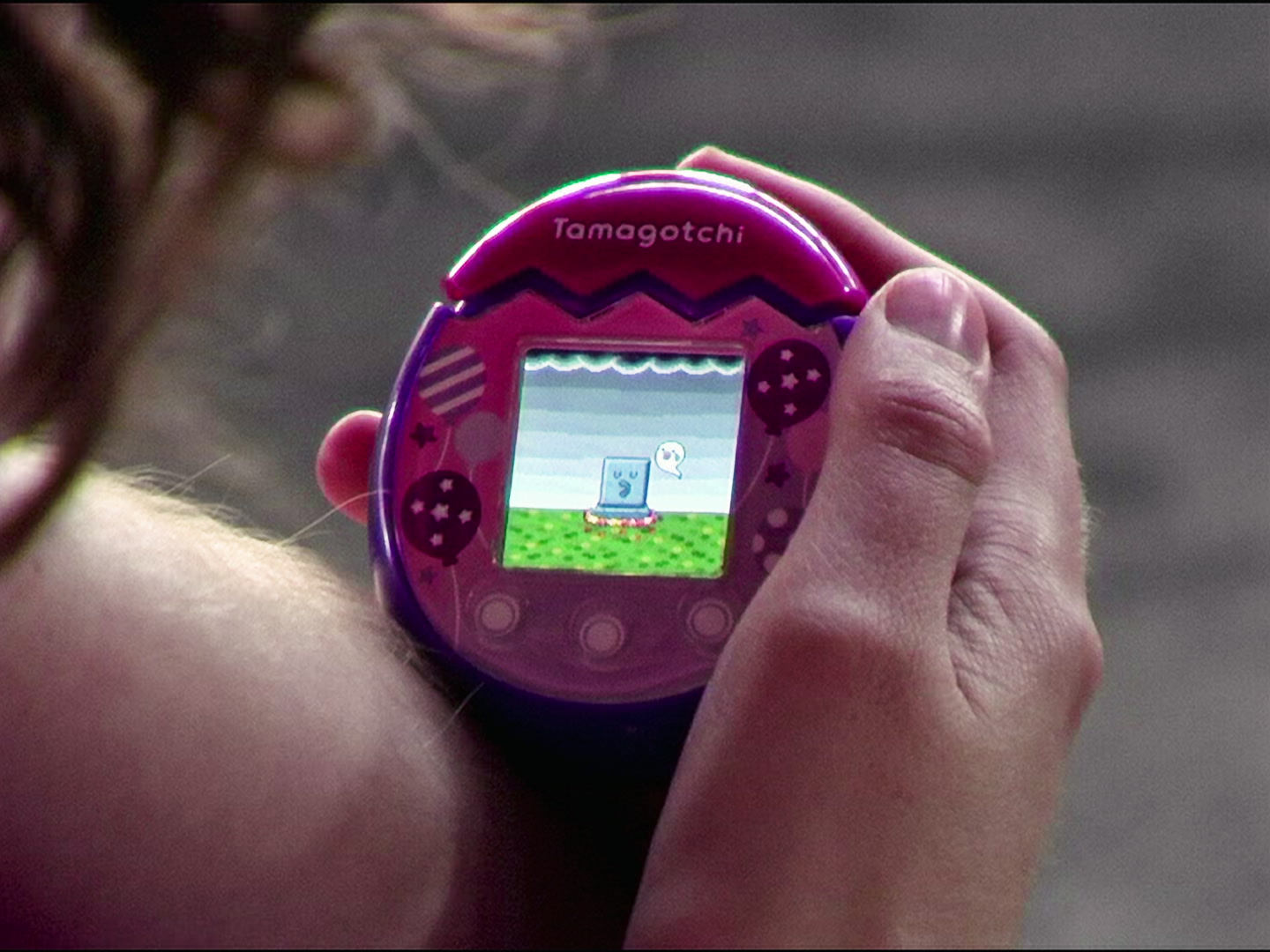 A hand holding a purple Tamagotchi with a gravestone on its screen